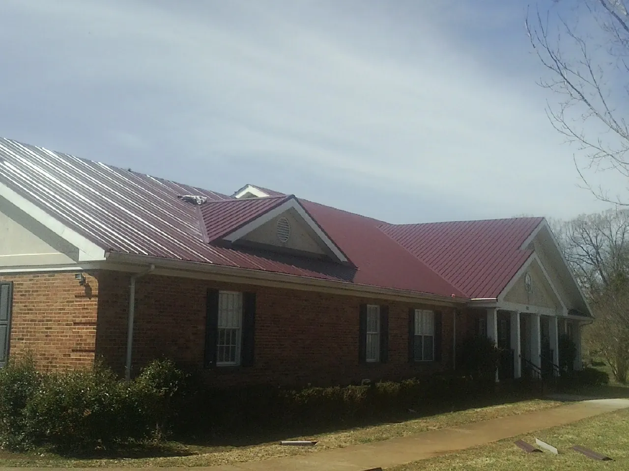 Red metal roof with gabled entries on a long brick building, from a Hail Damage Roof Repair job in Madill