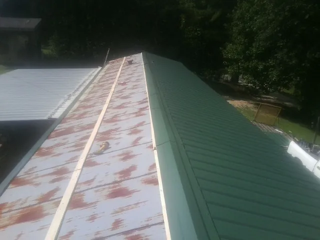 Old rusted panels beside newly installed green metal roofing — Wind Damage Roof Repair by Roofing Brothers in Madill