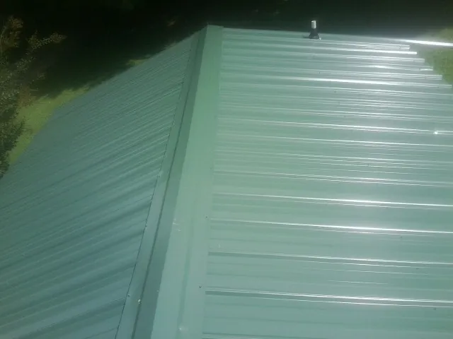 New green metal panels meeting at the ridge of a roof — Flat Roof Repair work by our crew in Madill