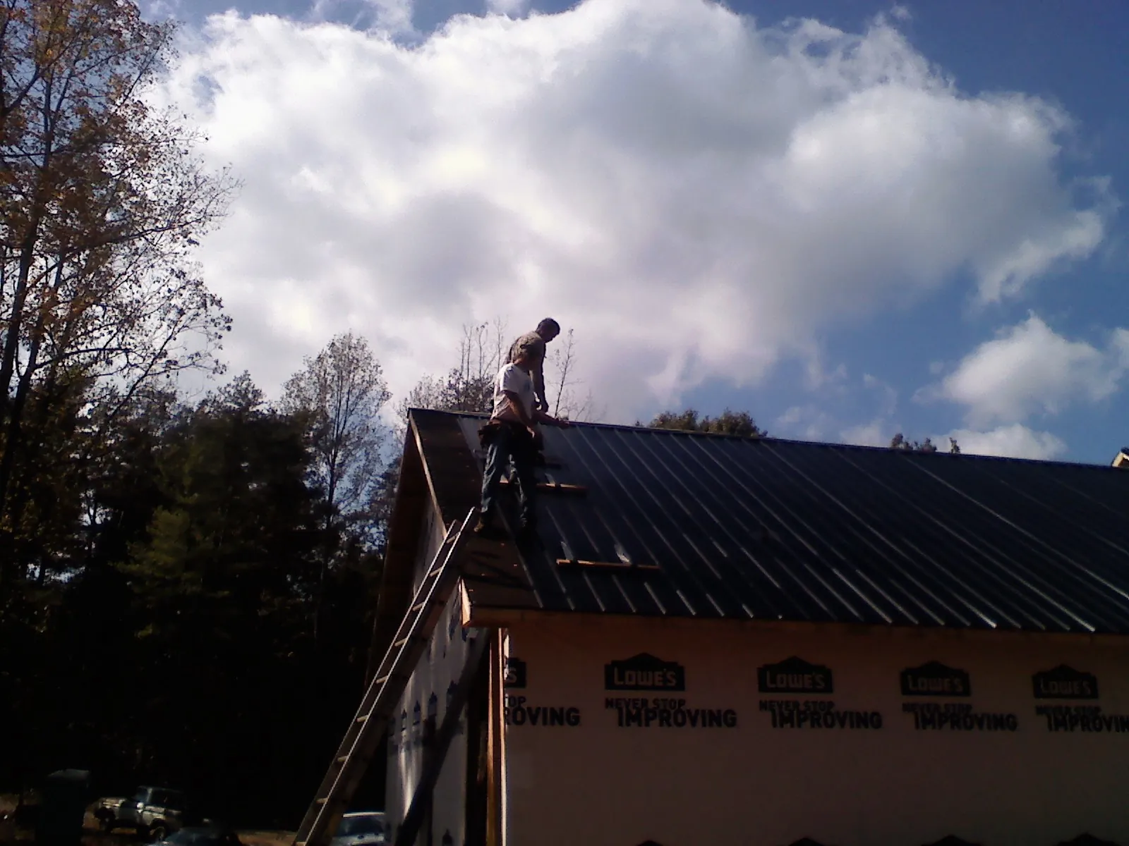 Roofer fastening dark metal panels high against a cloudy sky, from a Roof Inspection job in Madill