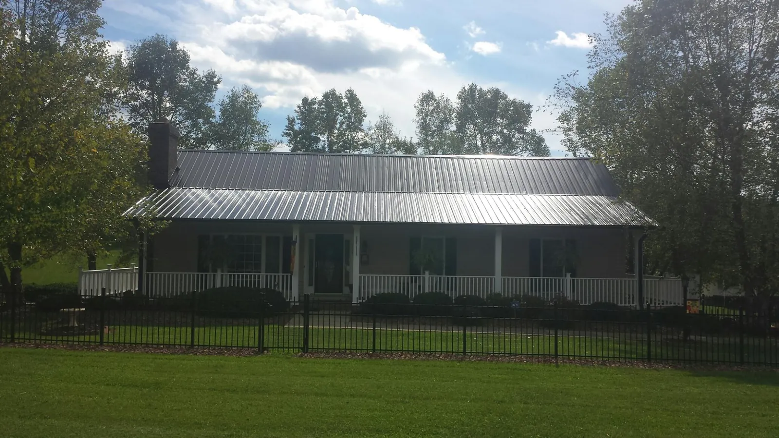 Gray metal roof on a brick ranch with a full width front porch — Gutter Guard Installation work by our crew in Madill