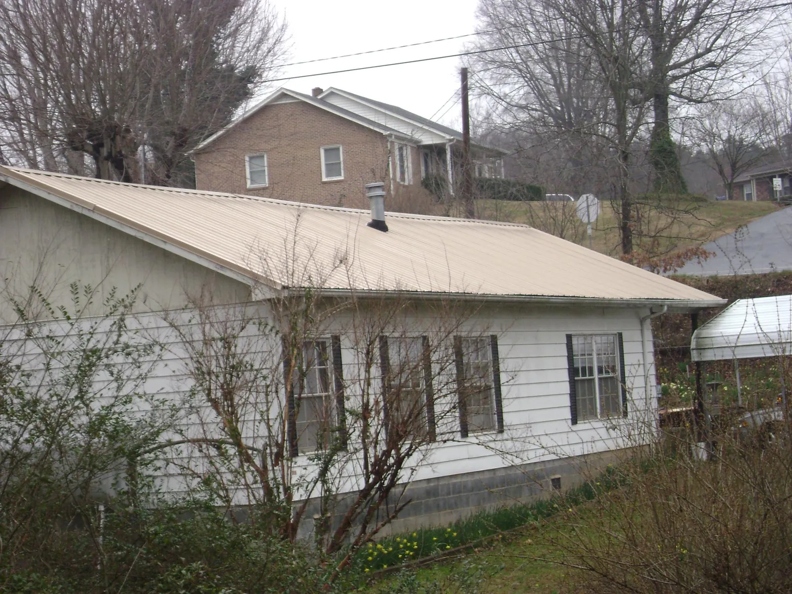 Tan metal roof on a white sided house set into a hillside — Commercial Roofing by Roofing Brothers in Madill