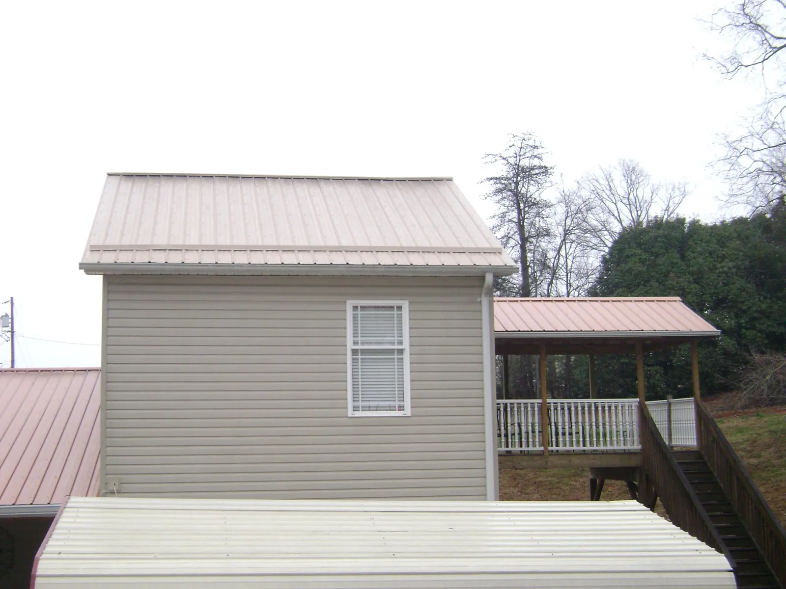 Tan metal roofs on a two story addition and attached porch, from a Roof Replacement job in Madill